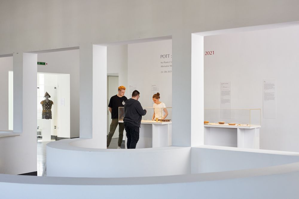Drei Besucher:innen stehen um eine Vitrine im Museum herum. Die ...